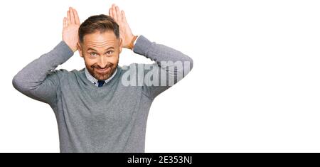 Beau homme d'âge moyen portant des vêtements d'affaires faisant des oreilles de lapin geste avec les mains palmiers regardant cynique et sceptique. concept de lapin de pâques. Banque D'Images