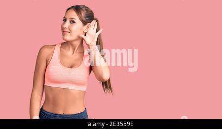 Jeune belle femme hispanique portant des vêtements de sport souriant de la main sur l'oreille écoutant une audition à la rumeur ou des potins. Concept de surdité. Banque D'Images