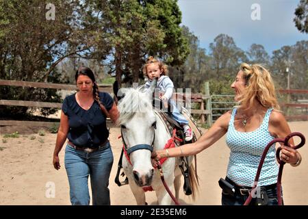 fille de 2 ans obtient sa première promenade sur un cheval, avec l'aide de l'entraîneur, et pour la sécurité sur une partie pour 2 ans Banque D'Images