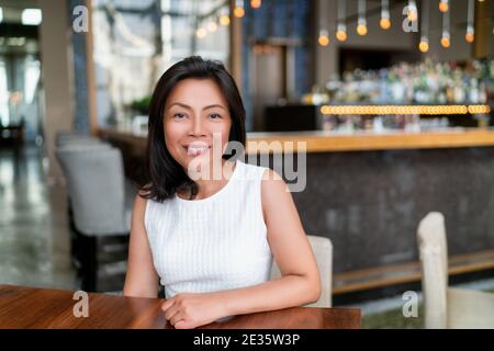 Femme d'affaires asiatique d'âge moyen souriant portrait. Bonne élégante femme d'affaires chinoise dans un cadre de restaurant chic Banque D'Images
