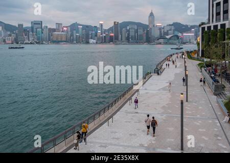Scène urbaine de front de mer avec des piétons marchant le long d'une promenade, Hong Kong skyline en arrière-plan. Banque D'Images