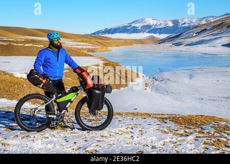 Homme barbu voyageur sur un vélo en hiver dans les montagnes. Voyage en hiver. Plateau de haute montagne Turgen-ASY, Kazakhstan Banque D'Images