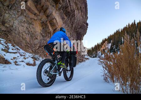 Un voyageur d'hiver sur un vélo dans les montagnes monte au sommet le long de la route parmi les falaises abruptes. Voyage en hiver. Gorge de Turgen, Kazakhstan Banque D'Images