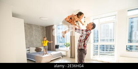 Un jeune père surjoyeux tenant deux enfants frères et sœurs, s'amusant ensemble à la maison, tête de tir. Papa excité jouant avec joyeux adorable petit Banque D'Images