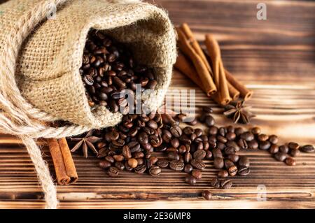 Sac en toile de jute épais avec grains de café saupoudrés sur un plan d'examen en bois brûlé avec bâtons de cannelle et étoiles anis. Copier l'espace Banque D'Images