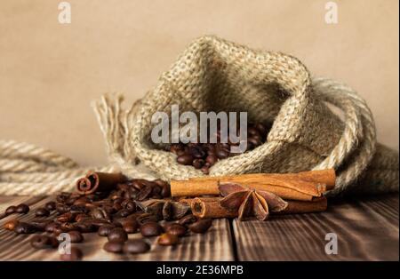 Sac en toile de jute épais avec grains de café saupoudrés sur un plan d'examen en bois brûlé avec bâtons de cannelle et étoiles anis. Copier l'espace Banque D'Images