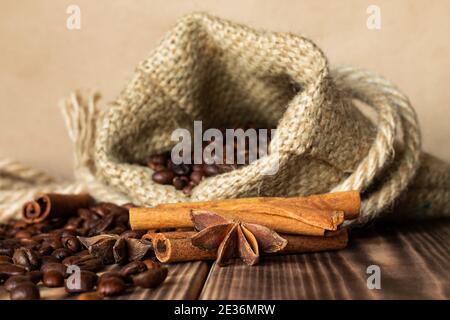 Sac en toile de jute épais avec grains de café saupoudrés sur un plan d'examen en bois brûlé avec bâtons de cannelle et étoiles anis. Copier l'espace Banque D'Images