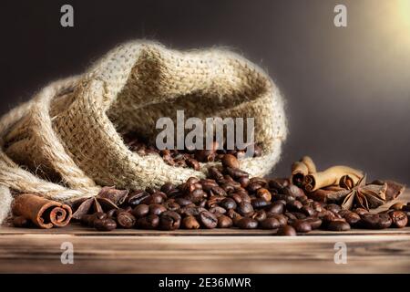 Sac en toile de jute épais avec grains de café saupoudrés sur un plan d'examen en bois brûlé avec bâtons de cannelle et étoiles anis. Copier l'espace Banque D'Images