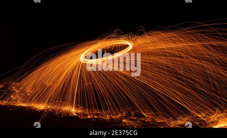 Swing Fire Swirl acier laine photographie de lumière avec réflexe dans l'eau longue exposition vitesse de mouvement style, belle ligne de feu. Banque D'Images