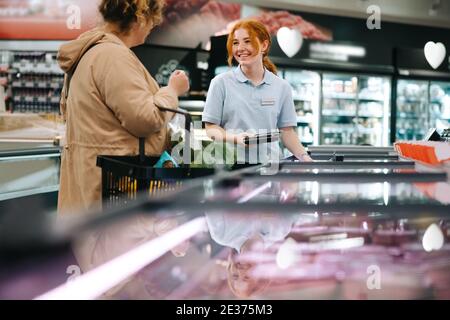 Assistant d'atelier aidant le client dans l'épicerie. Jeune travailleur aidant un acheteur dans un supermarché. Banque D'Images