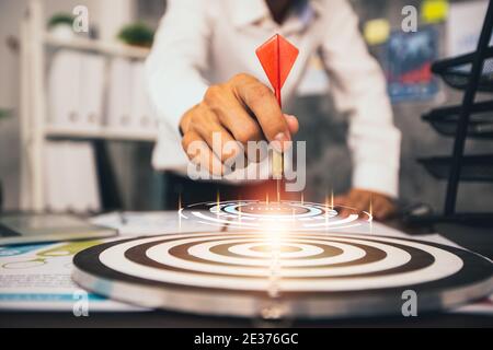 Gros plan de l'homme d'affaires tenant des fléchettes sur l'objectif avec le papier graphique financier avec ordinateur portable sur la table, réussite, succès et gagnant concept Banque D'Images