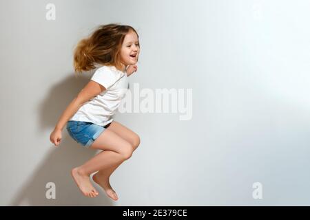 Une petite fille gaie qui saute. Enfant en short et T-shirt sur fond gris. Banque D'Images