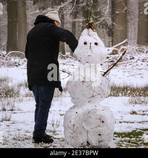 Duelmen, NRW, Allemagne. 17 janvier 2021. Un marcheur apporte une touche finale à un bonhomme de neige aux cheveux épiés. Une couche de neige fraîche est tombée la nuit, transformant la campagne du Muensterland en un pays merveilleux pour l'hiver pendant quelques jours. Credit: Imagetraceur/Alamy Live News Banque D'Images