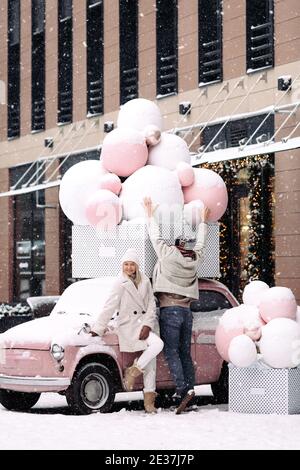 Couple romantique s'amusant en hiver debout près de l'ancien voiture rose rétro pendant les chutes de neige Banque D'Images