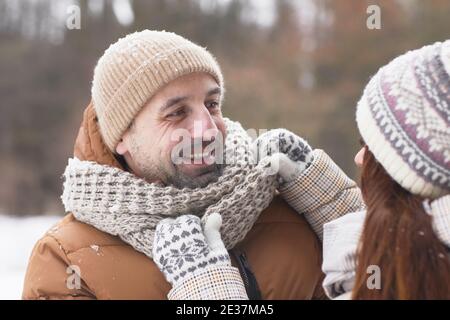 Portrait en gros plan d'un couple adulte heureux à l'extérieur en hiver avec une femme attentionnée portant une écharpe sur son mari, espace de copie Banque D'Images