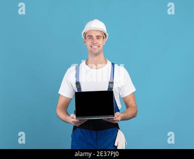 Smiling Foreman Guy en casque dur tenant un ordinateur portable avec noir Écran vide Banque D'Images