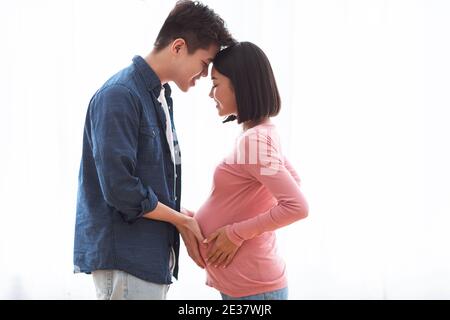 Un mari asiatique aimant touchant la femme enceinte et se tenant à la maison Banque D'Images