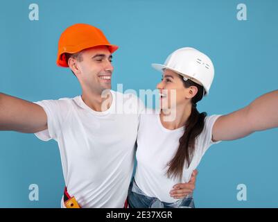 Un couple joyeux et enthousiaste dans des casques durs protecteurs qui prennent le contrôle de Selfie Arrière-plan bleu Banque D'Images