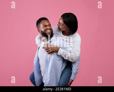 Romantique homme noir donnant à sa petite amie pigyback sur fond rose studio. Saint Valentin Banque D'Images