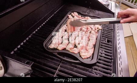 Cuisson de tranches de bacon sur un barbecue à gaz extérieur. Banque D'Images