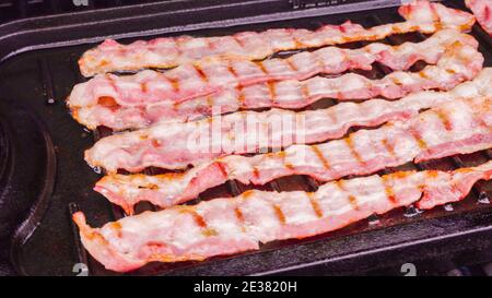 Cuisson de tranches de bacon sur un barbecue à gaz extérieur. Banque D'Images