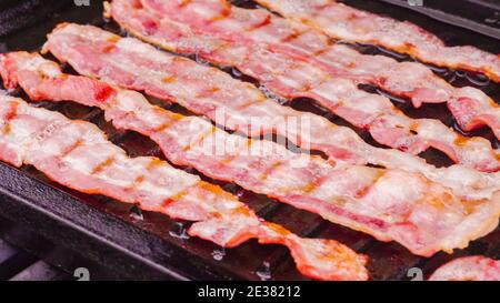 Cuisson de tranches de bacon sur un barbecue à gaz extérieur. Banque D'Images