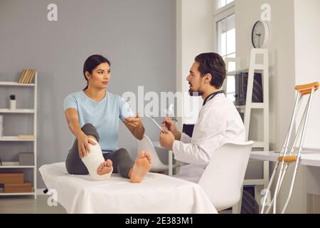 Jeune femme avec une jambe cassée parlant au médecin pendant la médecine enregistrement à l'hôpital Banque D'Images