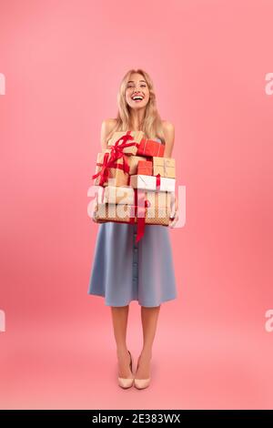 Portrait de pleine longueur de magnifique blonde dame avec pile de cadeaux de vacances sur fond rose studio. Fête des femmes Banque D'Images