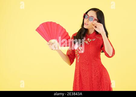 Porrtrait de belle jeune femme en robe rouge et lunettes de soleil utilisation du ventilateur de papier Banque D'Images