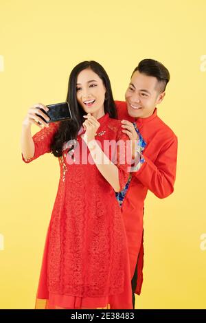 Beau jeune couple asiatique en robes traditionnelles posant pour selfie ou enregistrer des vidéos ensemble Banque D'Images