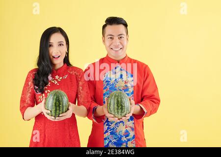 Portrait d'un jeune couple asiatique heureux dans le traditionnel Lunar New Costumes d'année contenant des pastèques fraîches et mûres Banque D'Images