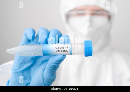 Médecin portant une combinaison jetable ou un vêtement de protection avec masque et sécurité google tenant un tube à essai avec vaccin. Banque D'Images
