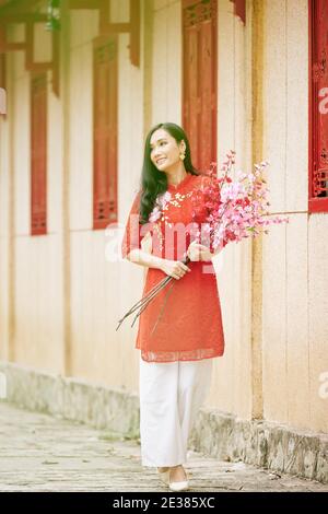 Jolie jeune femme vietnamienne en robe traditionnelle portant des pêches en fleur Succursales en plein air après avoir fêté le nouvel an chinois Banque D'Images