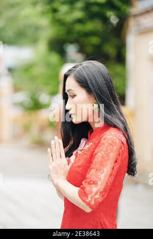 Jeune femme asiatique pensive en robe rouge priant à l'extérieur, la spiritualité et la religion cocenpt Banque D'Images