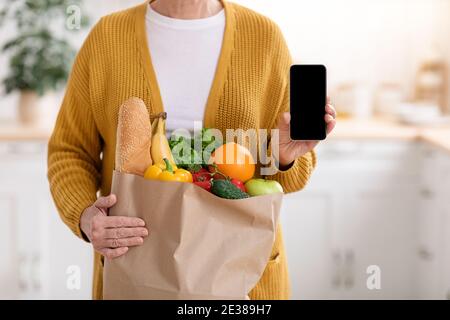 Écourté d'une femme avec un sac à provisions montrant un téléphone portable Banque D'Images