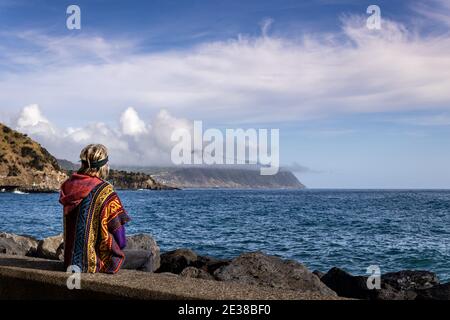 Femme assise au bord de l'océan Atlantique, temps calme, voyage seul, plein air. Banque D'Images