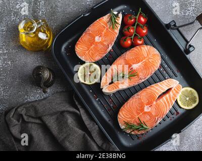 trois steaks de poisson crus truite, saumon et épices sur la poêle, fond sombre, Banque D'Images