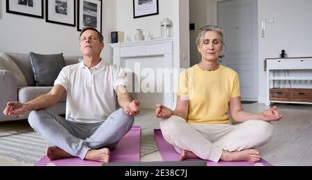 Sain conscient vieux mature couple des années 60 méditant faisant le yoga à la maison. Banque D'Images