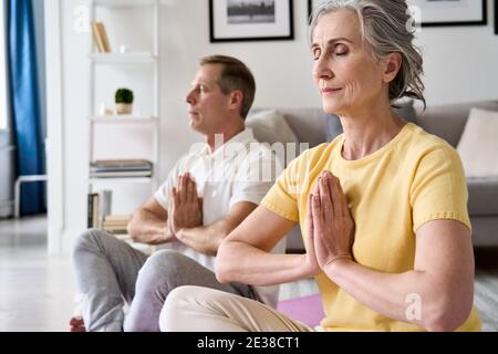 Calme sain vieux couple méditer avec les yeux fermés main namaste à la maison ensemble. Banque D'Images