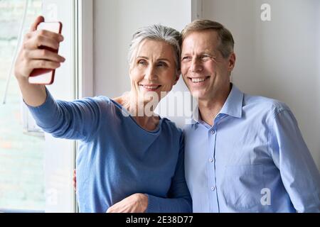 Heureux couple d'âge moyen tenant un smartphone pour prendre des photos de selfie à la maison. Banque D'Images