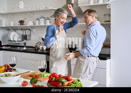 Joyeux vieux couple des années 50 ayant l'amusement dansant la cuisine ensemble dans la cuisine. Banque D'Images