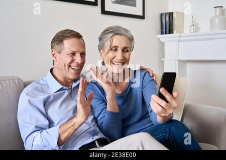 Un vieux couple heureux se faisant passer des mains pour passer un appel vidéo en ligne sur un téléphone portable. Banque D'Images