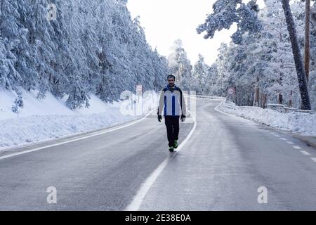 Un homme marche à travers le milieu d'une route sinueuse dans un paysage blanc solitaire enneigé par un froid jour d'hiver.concept de solitude, de liberté et de défi. Banque D'Images