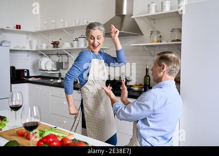 Joyeux couple d'âge moyen, plus âgé, s'amusant à danser et à cuisiner ensemble à la maison. Banque D'Images