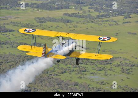 Un Boeing N2S Staarman des années 1940 en biplan aux couleurs de l'armée américaine, utilisant la fumée d'affichage. Banque D'Images