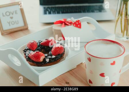 Un plateau avec une tasse de café latte, un bagel avec des fraises et des coeurs de bonbons, une boîte cadeau et une carte de vœux vierge, message Love You sur le lieu de travail avec la Banque D'Images