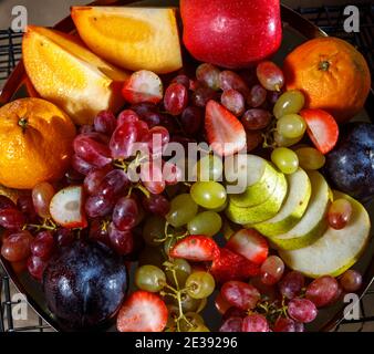 Assortiment de fruits en tranches, raisins roses et blancs, kiwi, pruneaux, persimmon, poire, pomme, orange, fraise sont sur un plateau. La vue du dessus. Banque D'Images