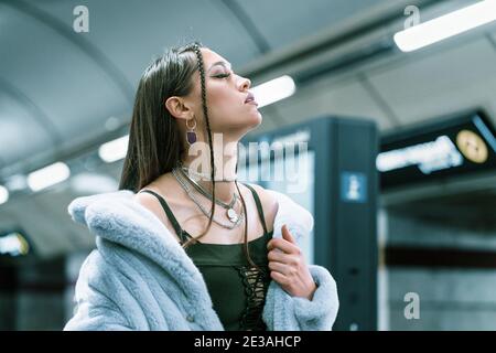 Mannequin de mode jeune femme en manteau de fourrure synthétique violet a élevé ses épaules marchant dans le métro ou plate-forme de métro. Femme avec maquillage de luxe, cheveux longs Banque D'Images