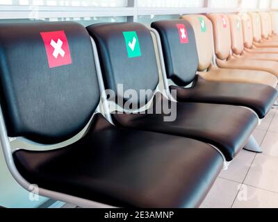 Chaises d'attente vides en gros plan avec signe de distance sociale, coche verte et croix rouge. Chaises noires avec symbole social de distance sur le siège Banque D'Images