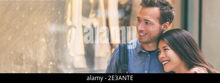 Couple multiracial magasiner ensemble en regardant les vêtements dans la fenêtre du magasin marchant dans la rue de la ville. Bonne femme asiatique embrassant homme caucasien mari Banque D'Images